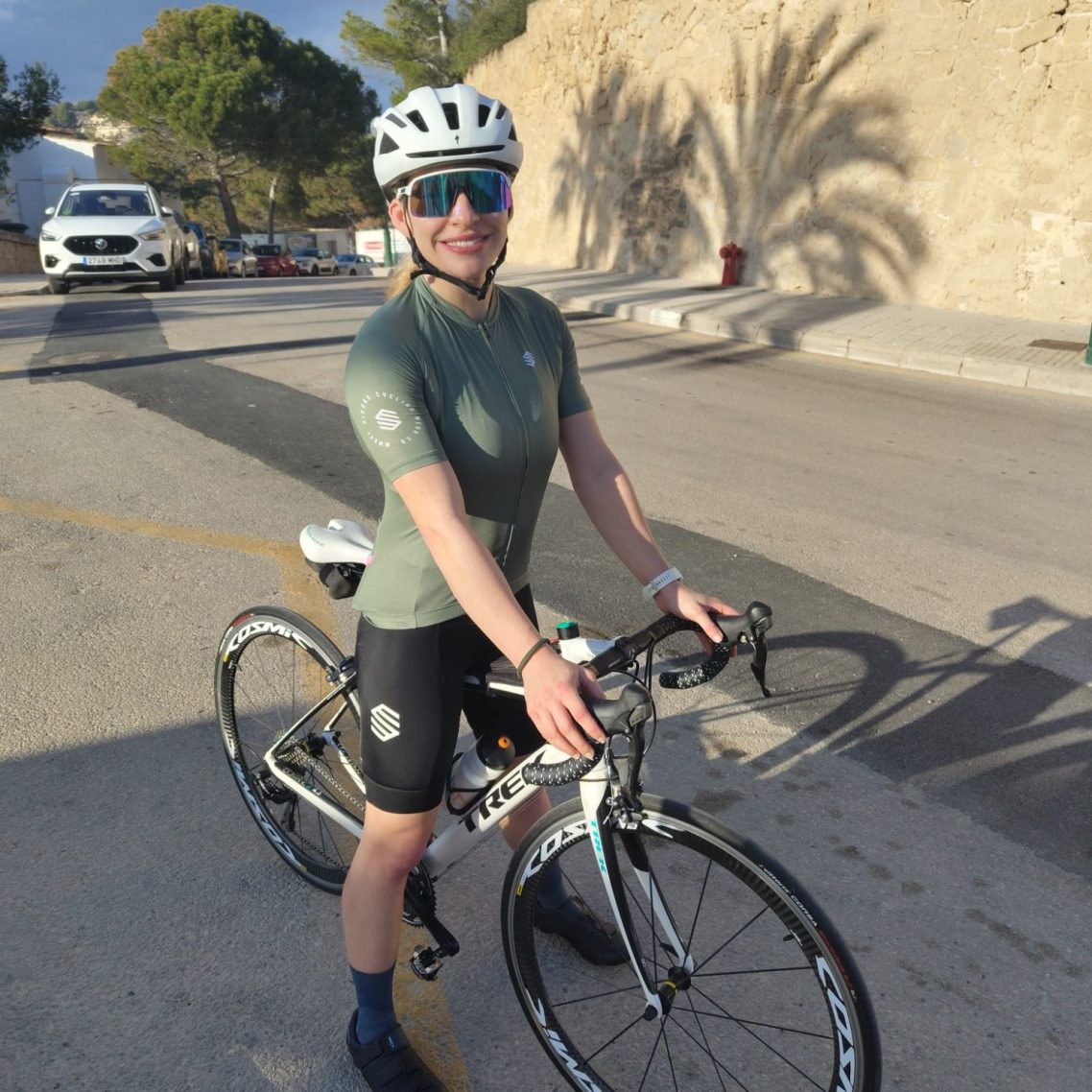 A cyclist in a green shirt poses beside a bike on a sunny street.