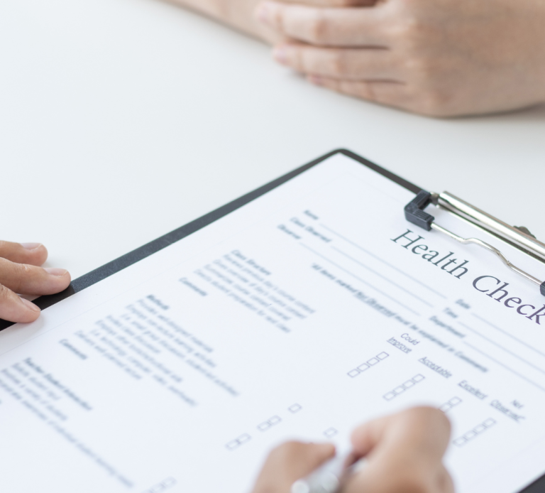 A person completing a health check form while another person observes.
